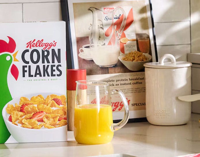 A box of Kellogg's Corn Flakes® and a small pitcher of orange juice.